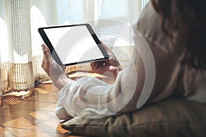 A woman holding black tablet pc with blank white desktop screen horizontally while laying down on the floor with