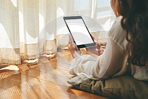 A woman holding black tablet pc with blank white desktop screen while laying down on the floor with feeling