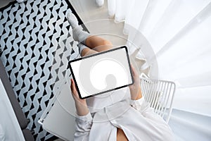 A woman holding black tablet pc with blank white desktop screen while sitting in bedroom with feeling