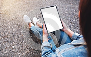 A woman holding a black tablet pc with blank white screen while sitting in the outdoors street