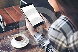 A woman holding black tablet pc with white blank screen and coffee cup on table background