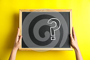 Woman holding blackboard with question mark on yellow background