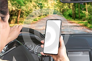 Woman holding blank screen cell phone while driving car. Female driver hand on steering wheel, checking out her smartphone in