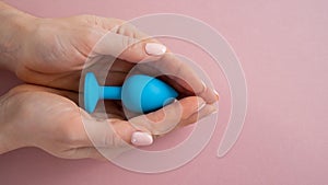 A woman is holding a blue anal plug on a pink background. Adult toy for alternative sex