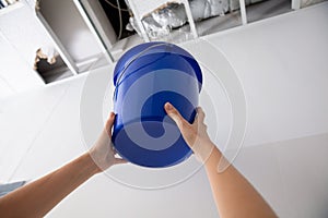 Woman Holding A Blue Bucket Under The Leak Ceiling