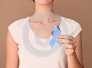 Woman holding blue ribbon on color background. Prostate cancer awareness concept