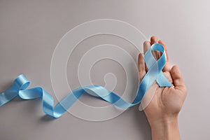 Woman holding blue ribbon on light background. Prostate cancer awareness concept