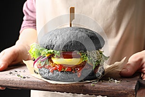 Woman holding board with tasty black vegetarian burger