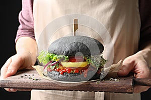 Woman holding board with tasty black vegetarian burger