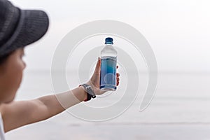 Woman holding bottle mineral water in her hand on the beach.