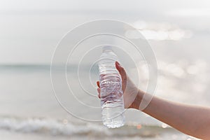 Woman holding bottle mineral water in her hand on the beach.