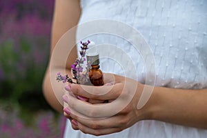 Woman holding bottle with natural essential oil in lavender field. Selective focus