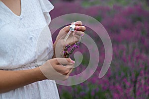 Woman holding bottle with natural essential oil in lavender field. Selective focus