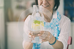 Woman holding bottle with water lemon and mint in kitchen