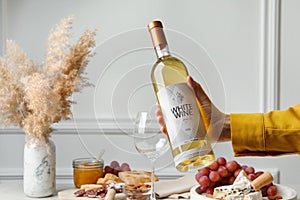 Woman holding bottle of white wine at table with snacks, closeup