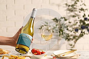 Woman holding bottle of wine over table with different snacks, closeup