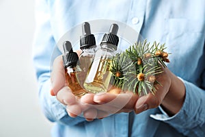 Woman holding bottles of essential oils and fir branches on white background