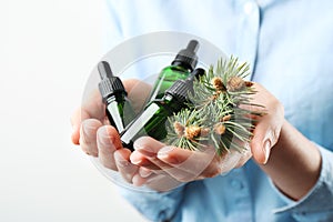Woman holding bottles of essential oils and fir branches on white background