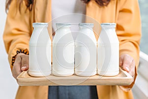 Woman holding bottles of pasteurized yogurt milk in white label color in wooden tray photo