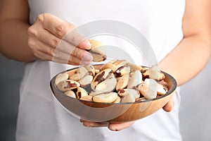 Woman holding bowl with Brazil nuts on grey background