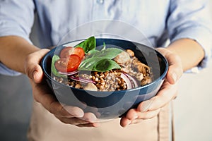 Woman holding bowl of delicious buckwheat porridge with vegetables and mushrooms