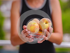 woman holding bowl of fresh peaches in her hands while standing in garden