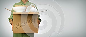 Woman holding box with household items for donations on gray background