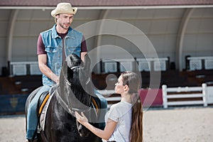 Woman holding bridle while handsome man in cowboy hat sitting on horseback