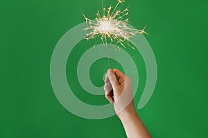 Woman holding bright burning sparkler on green background, closeup