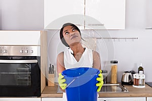 Woman Holding Bucket While Water Droplets Leak From Ceiling