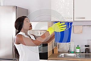 Woman Holding Bucket While Water Droplets Leak From Ceiling