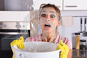 Woman Holding A Bucket While Water Droplets Leak From Ceiling