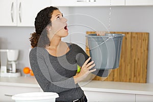 Woman holding bucket while water droplets leak from ceiling