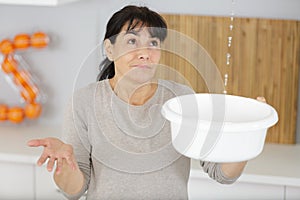 woman holding bucket while water droplets leak from ceiling