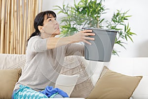 woman holding bucket while water droplets leak from ceiling