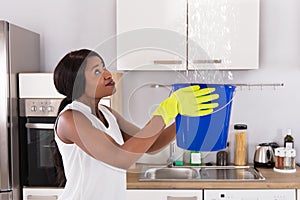 Woman Holding Bucket While Water Droplets Leak From Ceiling