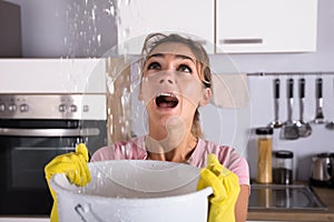 Woman Holding A Bucket While Water Droplets Leak From Ceiling