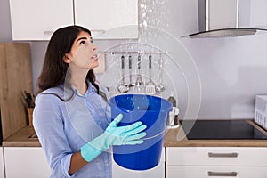 Woman Holding Bucket While Water Droplets Leak From Ceiling