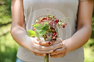 Woman holding bunch with fresh wild strawberries on blurred background, closeup