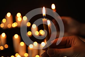 Woman holding burning candle in darkness against blurred background, closeup.