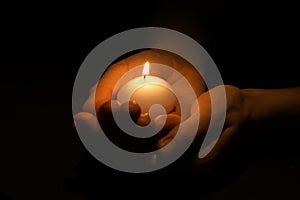 Woman holding burning candle in hands on black background, closeup