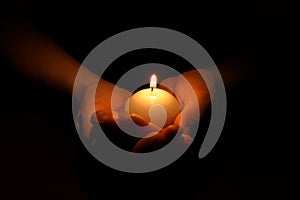 Woman holding burning candle in hands on black background