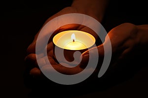 Woman holding burning candle in hands on black background, closeup