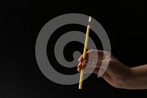 Woman holding burning church candle on black background, closeup