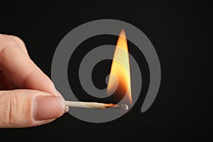 Woman holding burning match on black background