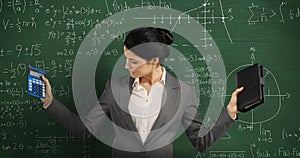 Woman holding calculator and notebook standing and looking around in front of chalkboard
