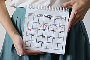 Woman holding calender with marked missed period. Unwanted pregnancy, woman`s health and delay in menstruation.