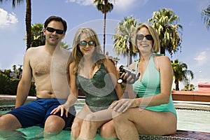 Woman holding camcorder with couple at swimming pool portrait.