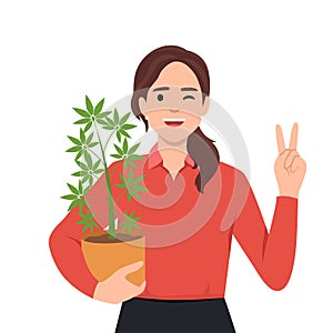 Woman holding cannabis plant in pot and giving peace sign as she is supporting the use of cannabis. Weed or marijuana