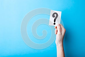 Woman holding card with question mark on color background. Paper note with question mark or sign against blue background. Ask or b